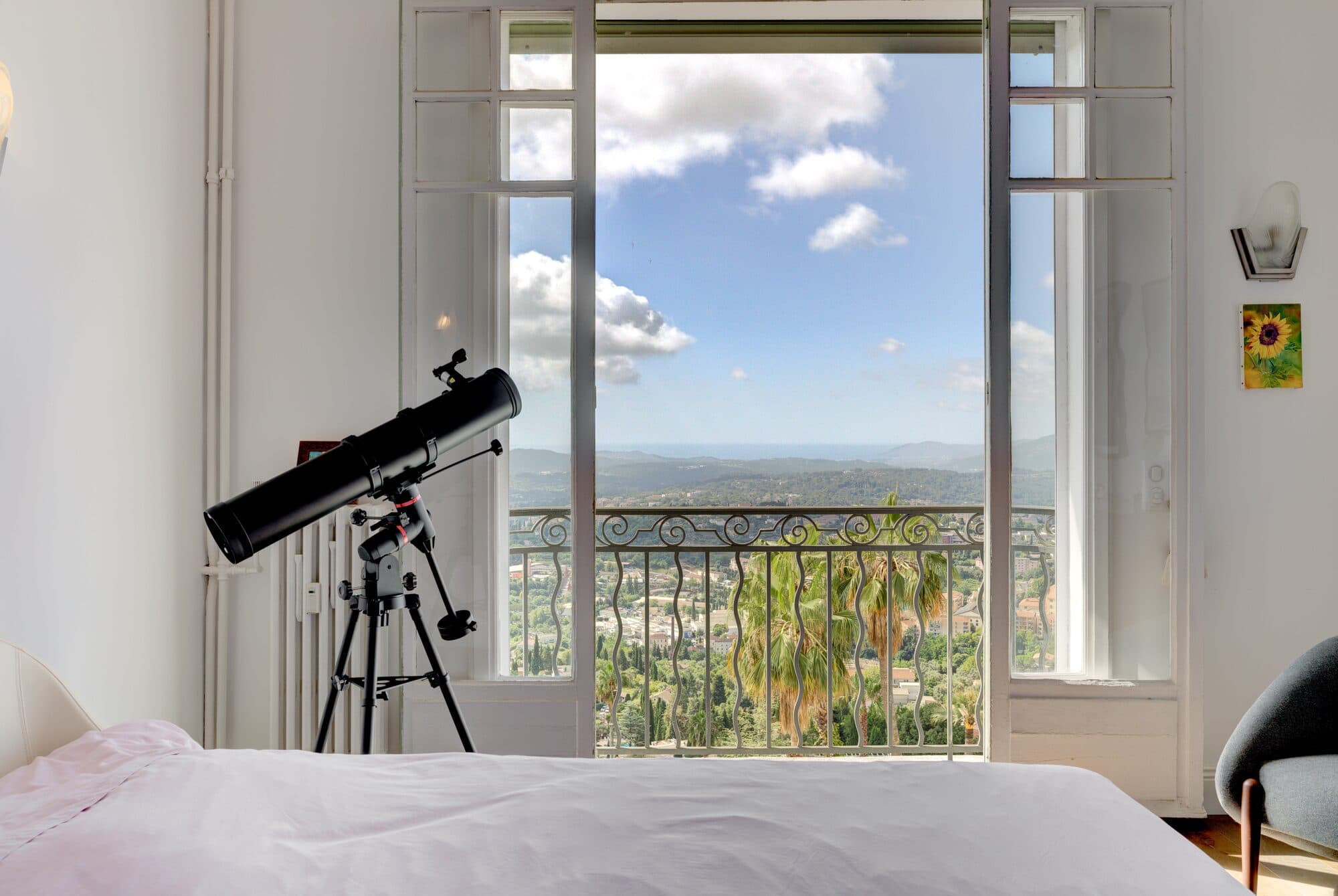 A bedroom window opening onto the valley, with a telescope in the foreground