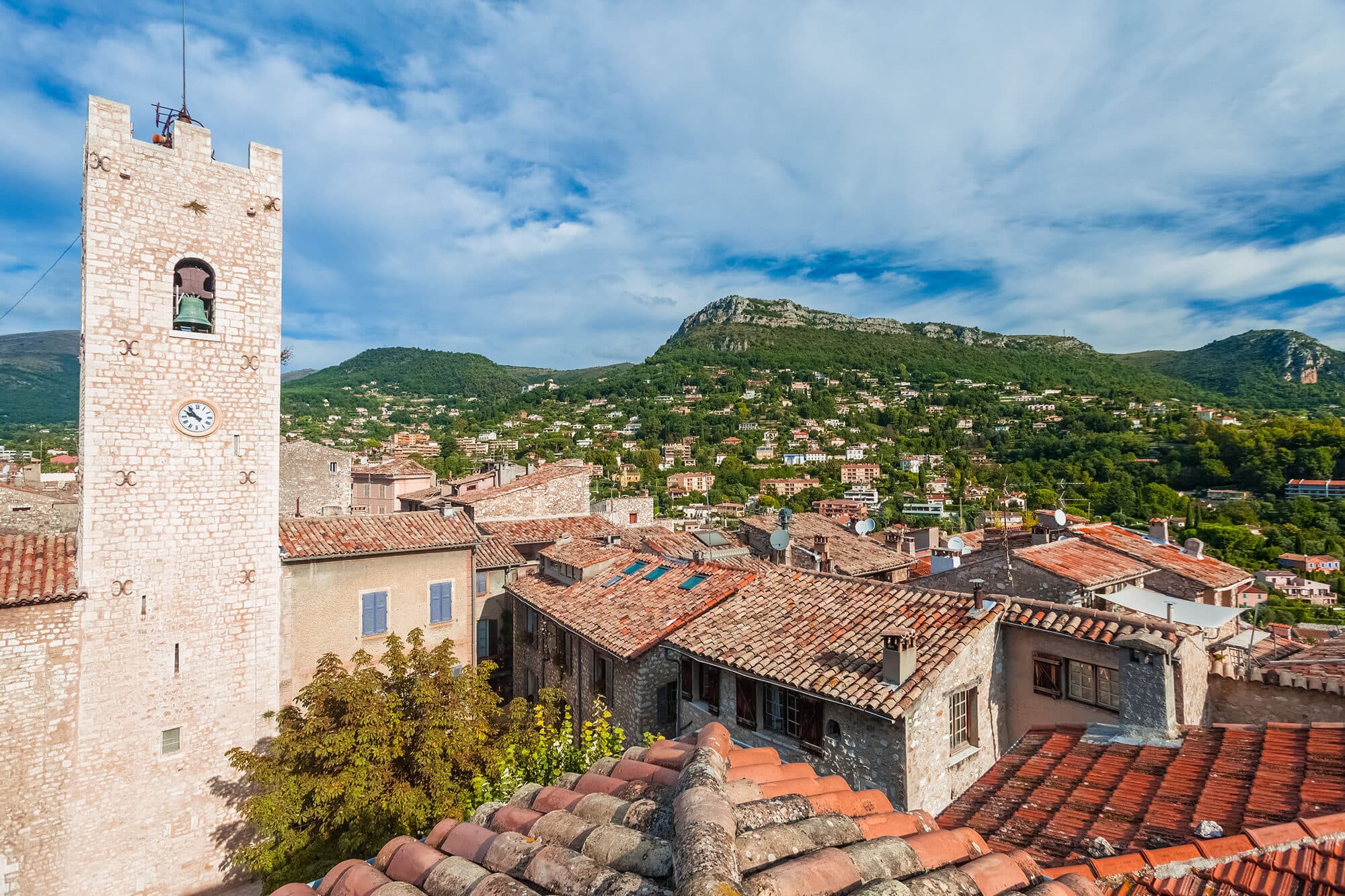 The clock tower of Vence and the tiled roofs of the old village, set against the wooded baous