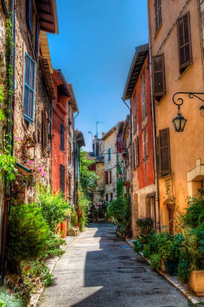 A sloping lane in the old town of Vence, with coloured façades and potted plants